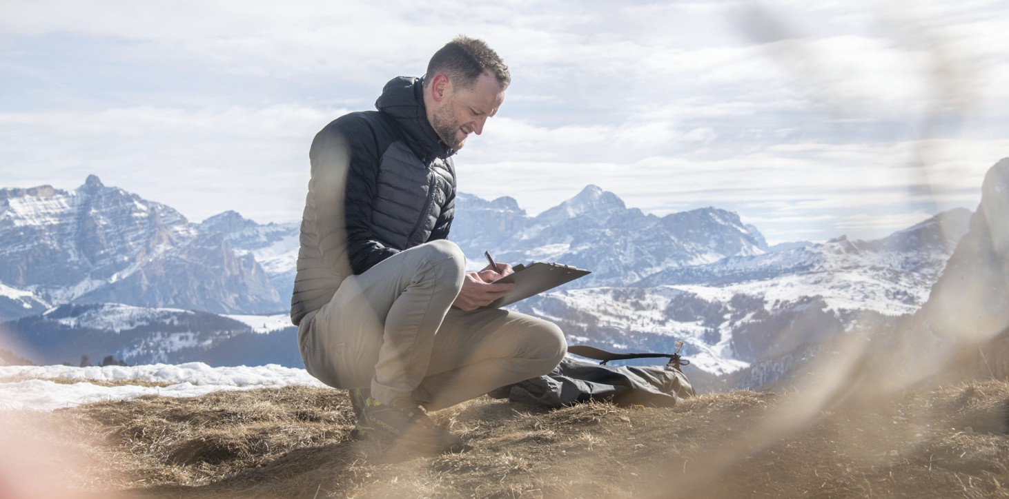 Das Bild zeigt Paul Felix Rigo in den Dolomiten. Er schreibt gerade etwas auf und wirkt nachdenklich – wie es für einen Coach typisch ist.