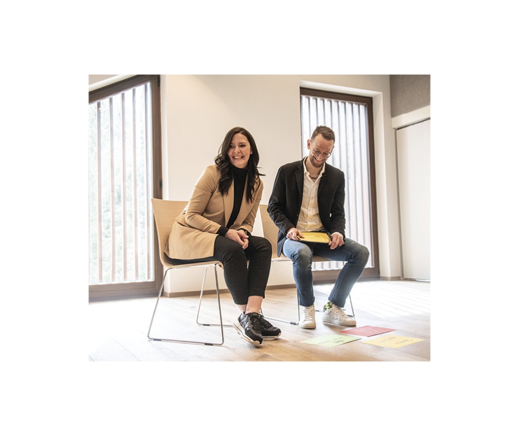 rigofree | professionelle Business Coachings direkt in Deinem Büro, Firmensitz und Unternehmen. Das Bild zeigt Paul beim Coaching einer Frau in einem Seminarraum. Auf dem Boden liegen beschriebene Papiere.